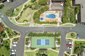 Ein Luftbild eines Wohngebiets mit Schwimmbad, Tennisplatz und umliegender Grünfläche.