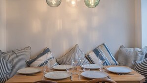 A dining area with a wooden table set for six, three hanging pendant lights, and striped pillows on a sofa. - Charming Cornish Cottage in the heart of St Agnes (St Agnes)