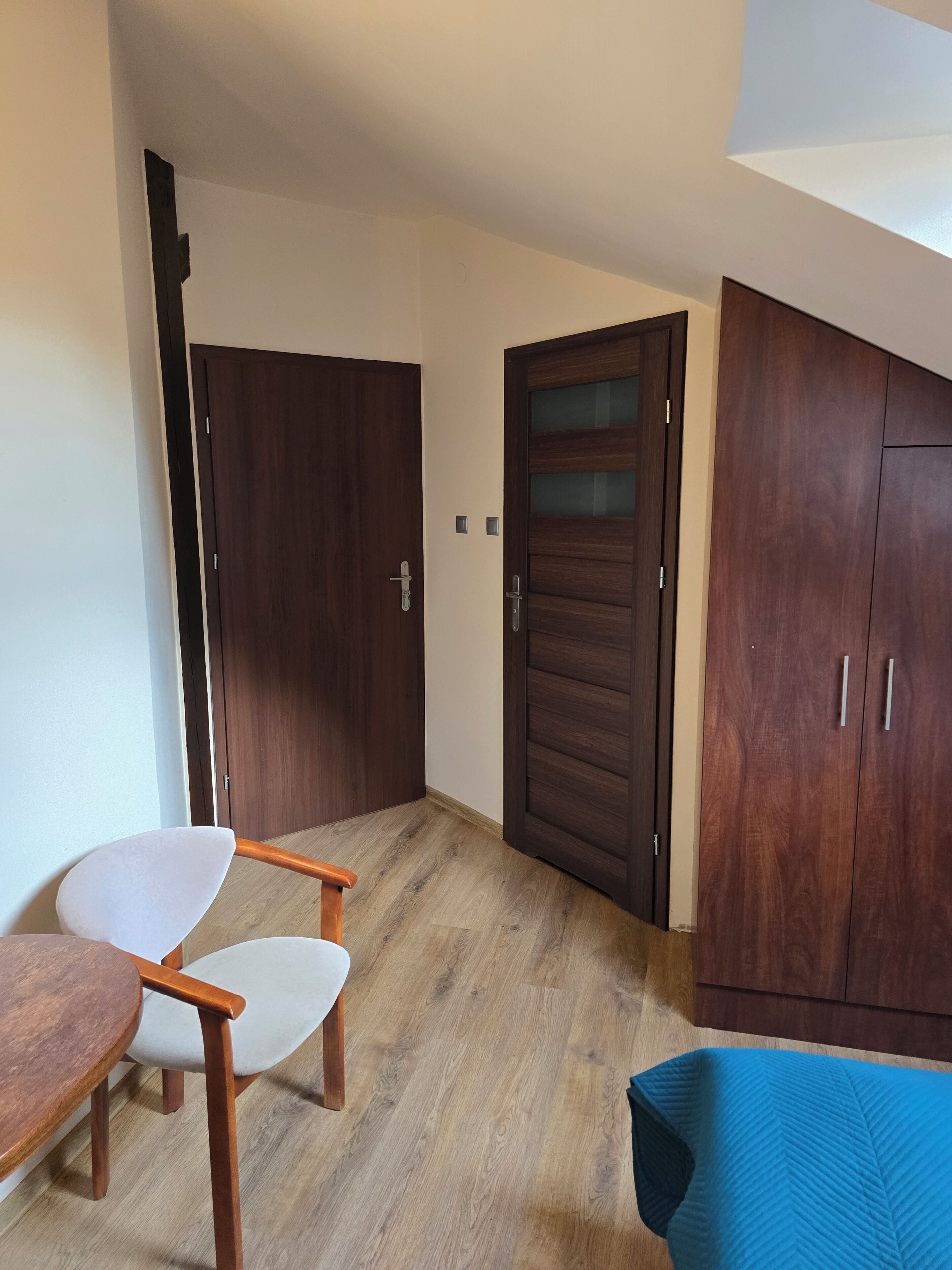 A room with a wooden floor, a white chair, a wooden table, and a wardrobe with two doors.