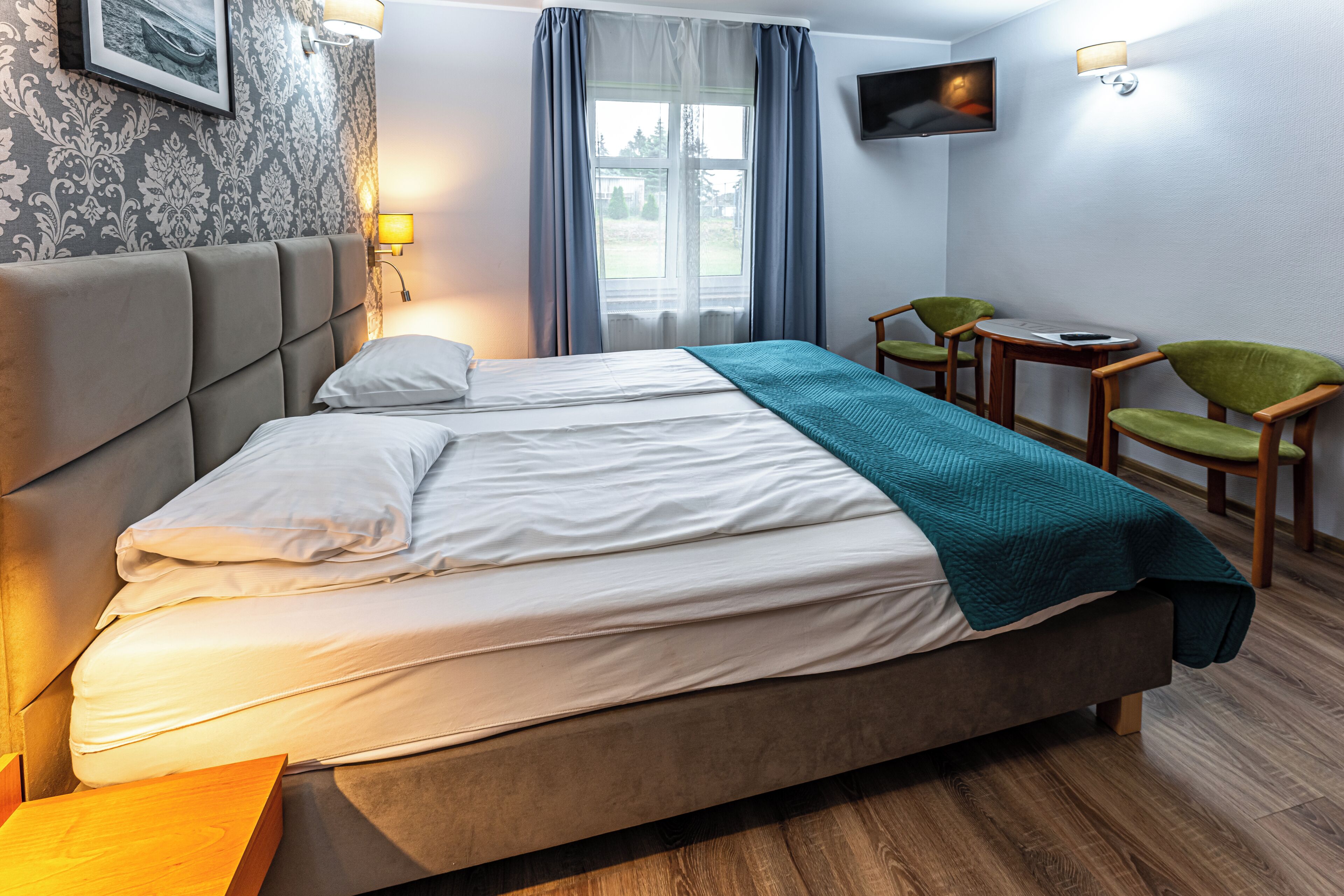 A hotel room with a bed, a desk, two chairs, a TV, and a window with curtains.