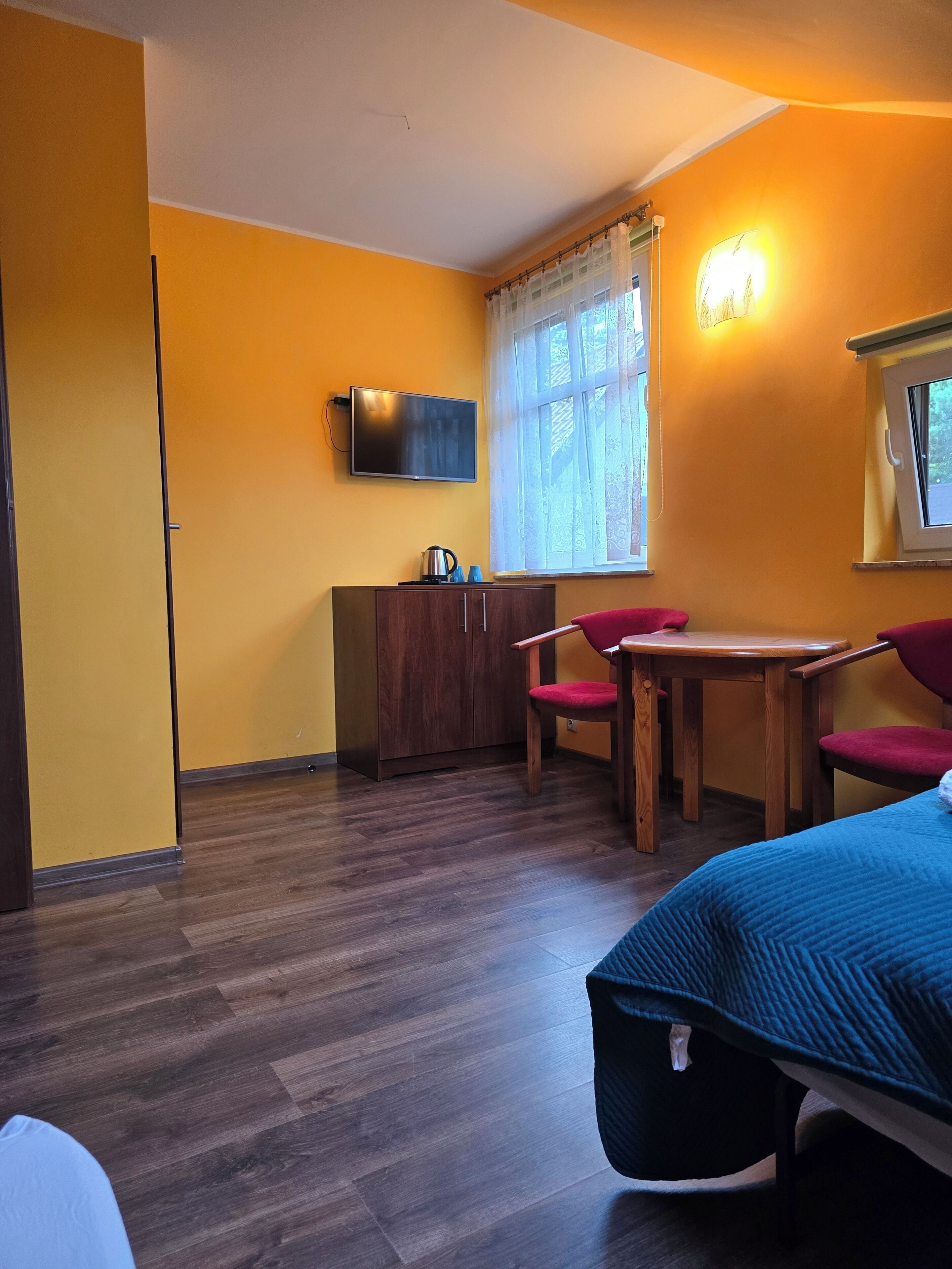 A room with a bed, a desk, a chair, a television, and a window with curtains.
