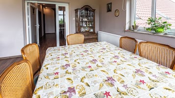 Comedor con una mesa dispuesta para cuatro, un aparador de madera, sillas de mimbre y una ventana con vistas a un tejado de tejas rojas.