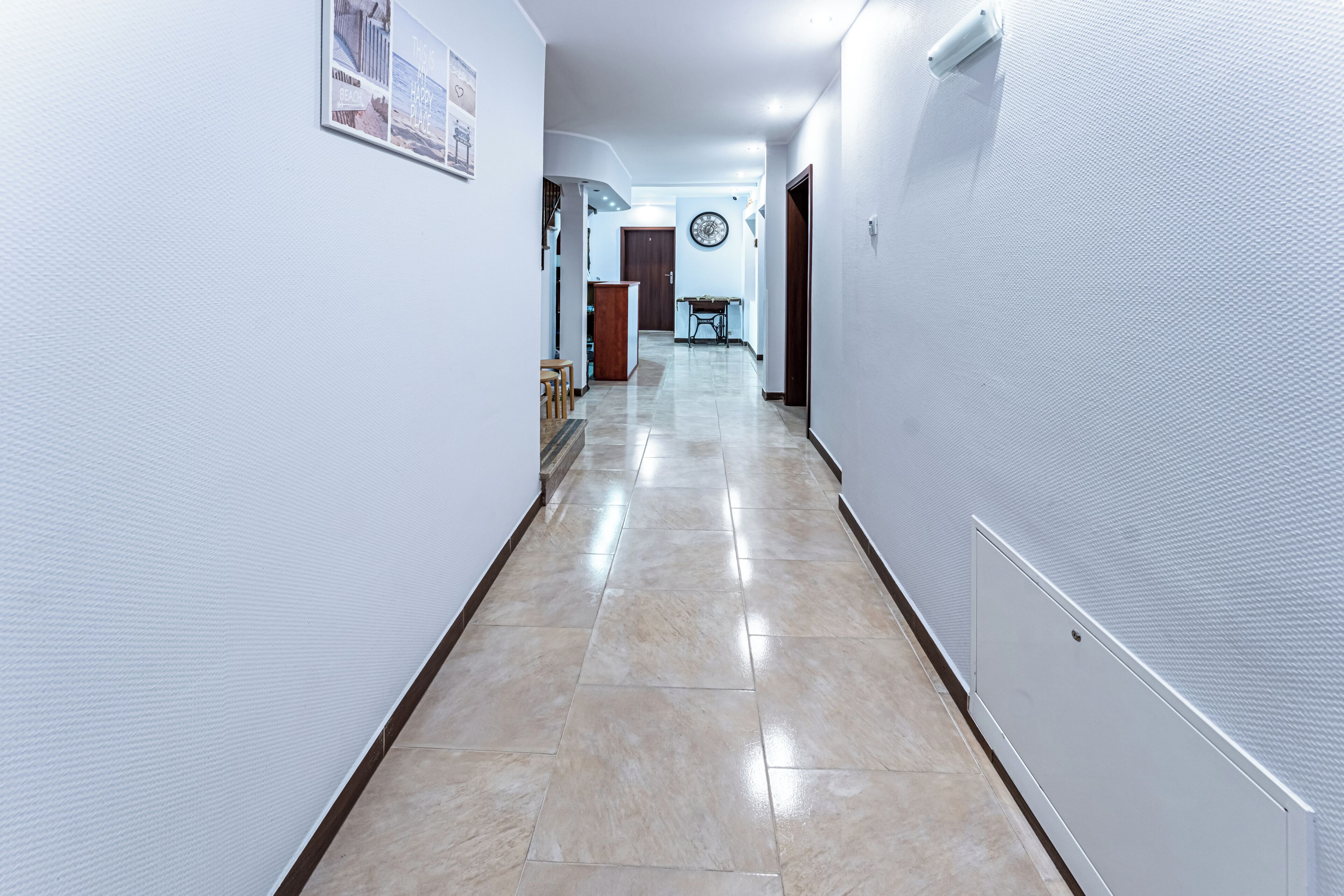 Um corredor com soalho em azulejos, paredes brancas e uma porta de madeira no final.