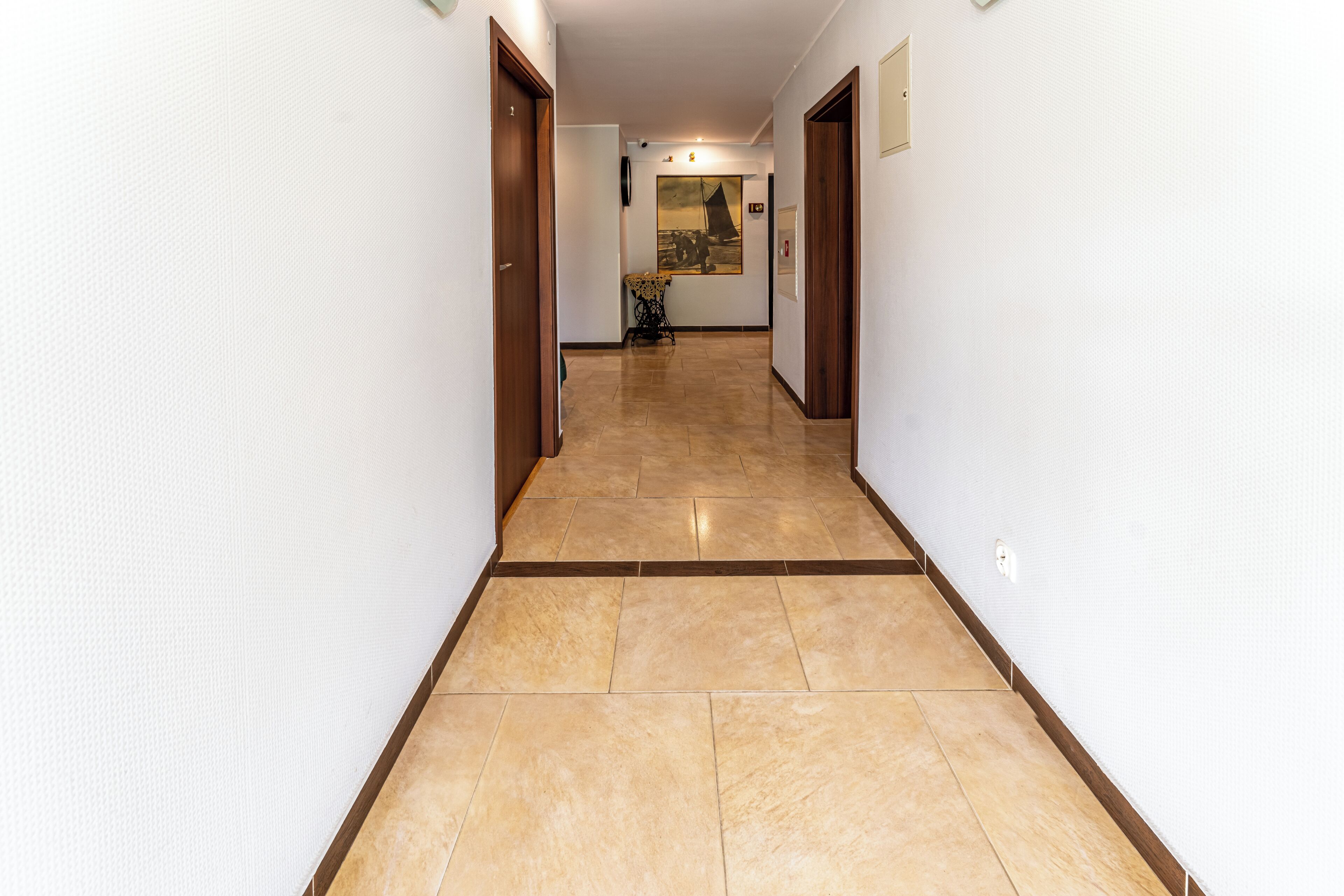 Un pasillo con suelo de baldosas, puertas de madera y un cuadro en la pared.