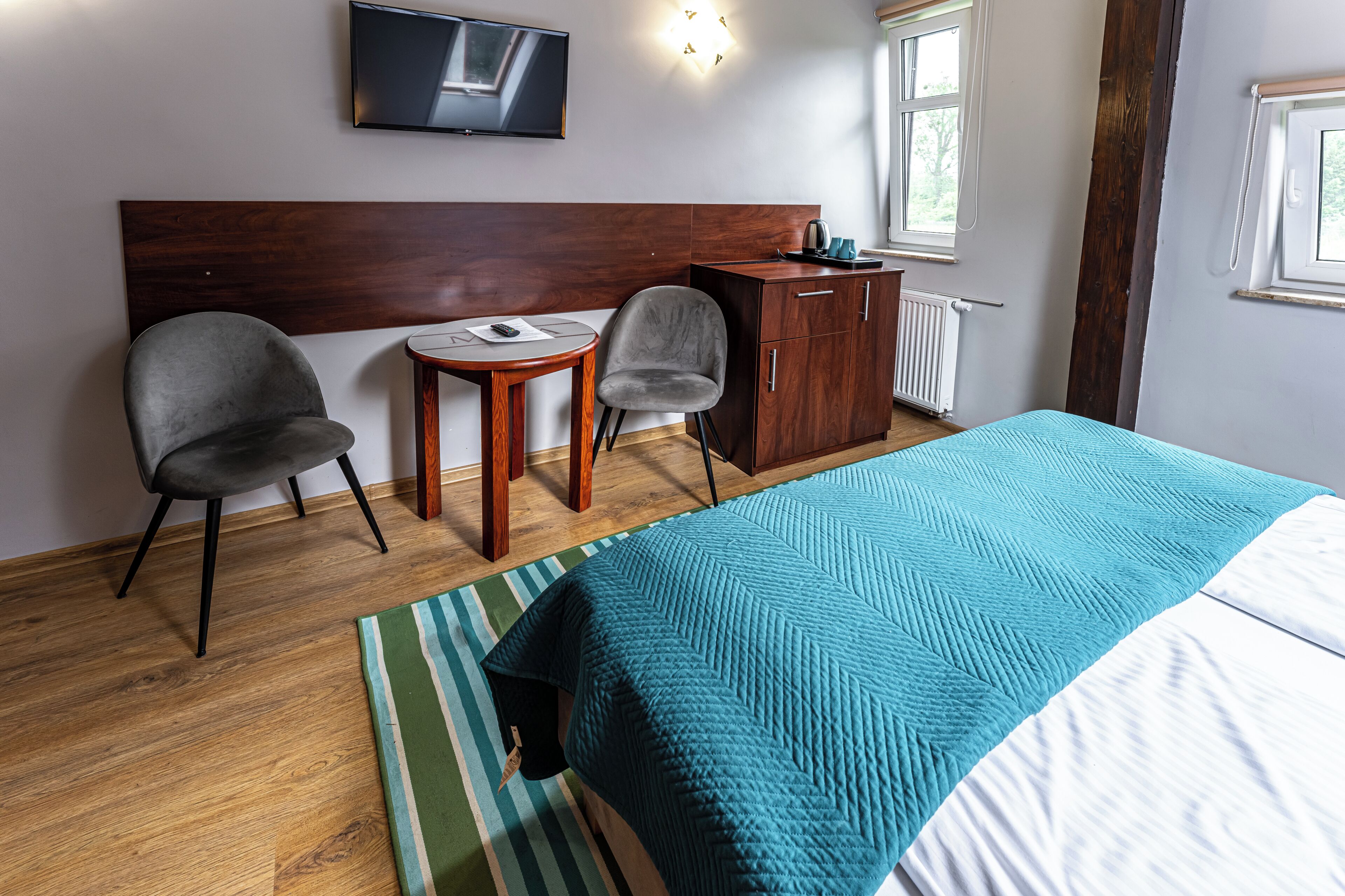 A hotel room with a bed, two chairs, a small table, a TV, and a wardrobe.