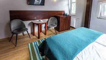A hotel room with a bed, two chairs, a small table, a TV, and a wardrobe.