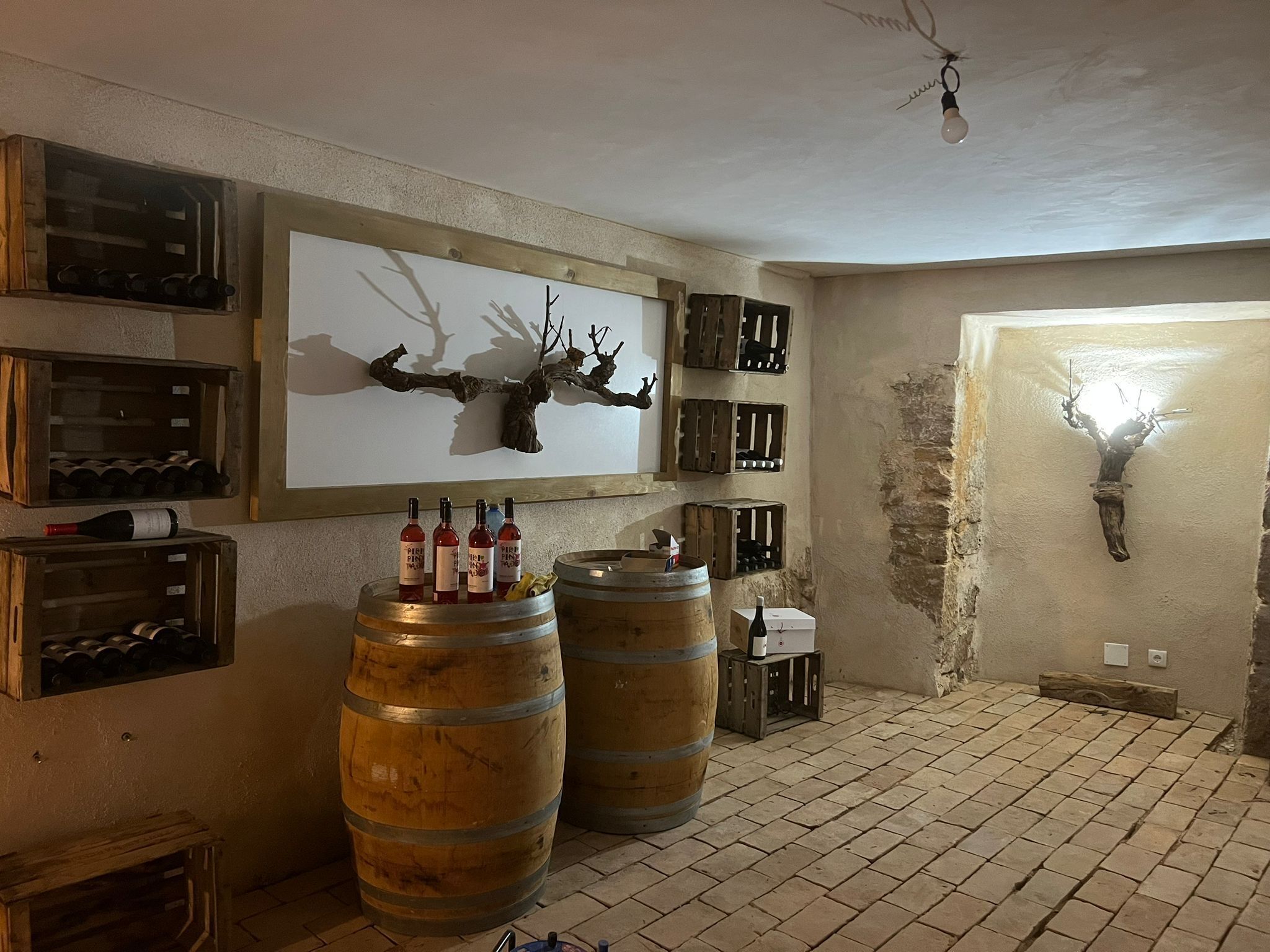 Una habitación rústica con barriles de madera, botellas de vino y cajas en las paredes.