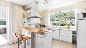 Una cocina moderna con una isla central, taburetes de bar, horno empotrado y un amplio ventanal con vistas a zonas verdes.