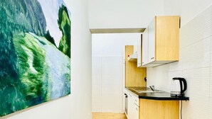 A narrow kitchen with wooden cabinets, a black countertop, and a painting of a landscape on the wall. - Urban 10BR Retreat Near Rathausplatz (Vienna)