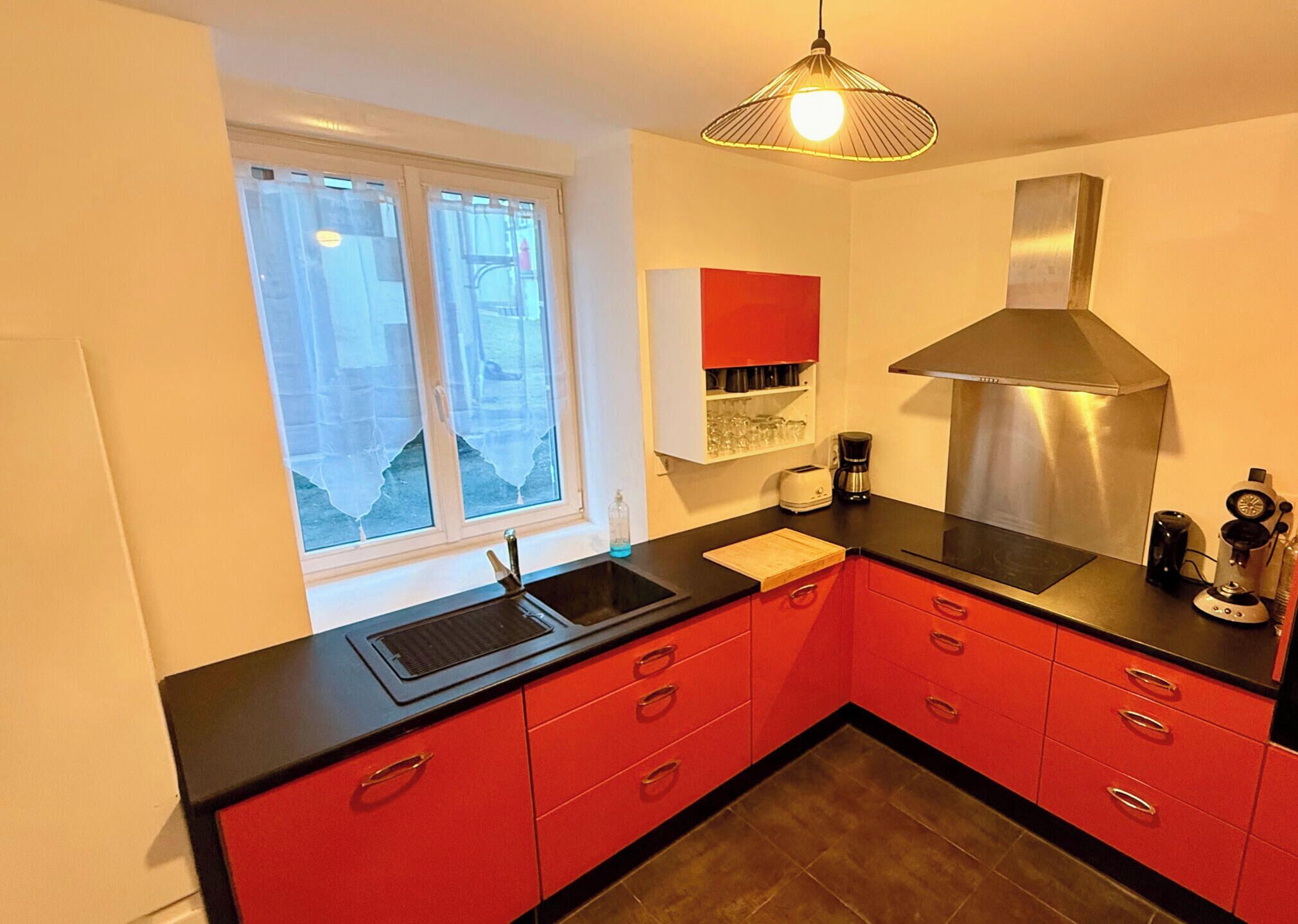 Una cocina moderna con armarios rojos, una campana extractora de acero inoxidable, una encimera negra y un ventanal con vistas al exterior.