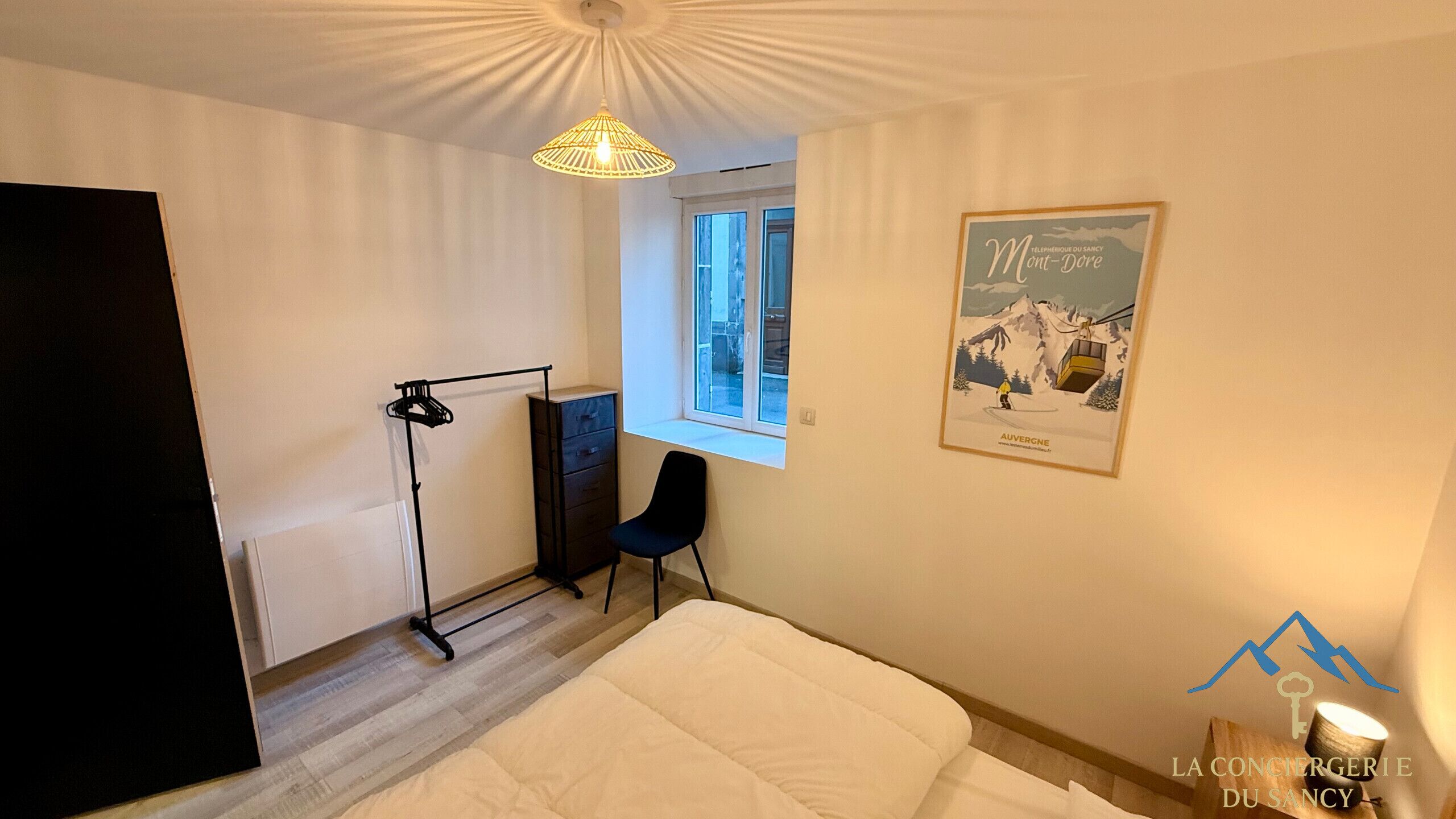 A bedroom with a bed, a desk, a chair, a window, and a poster on the wall.