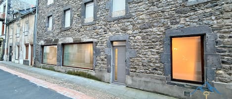 Un edificio de piedra con ventanas amplias, una puerta y un símbolo de llave que indica servicio de conserjería.