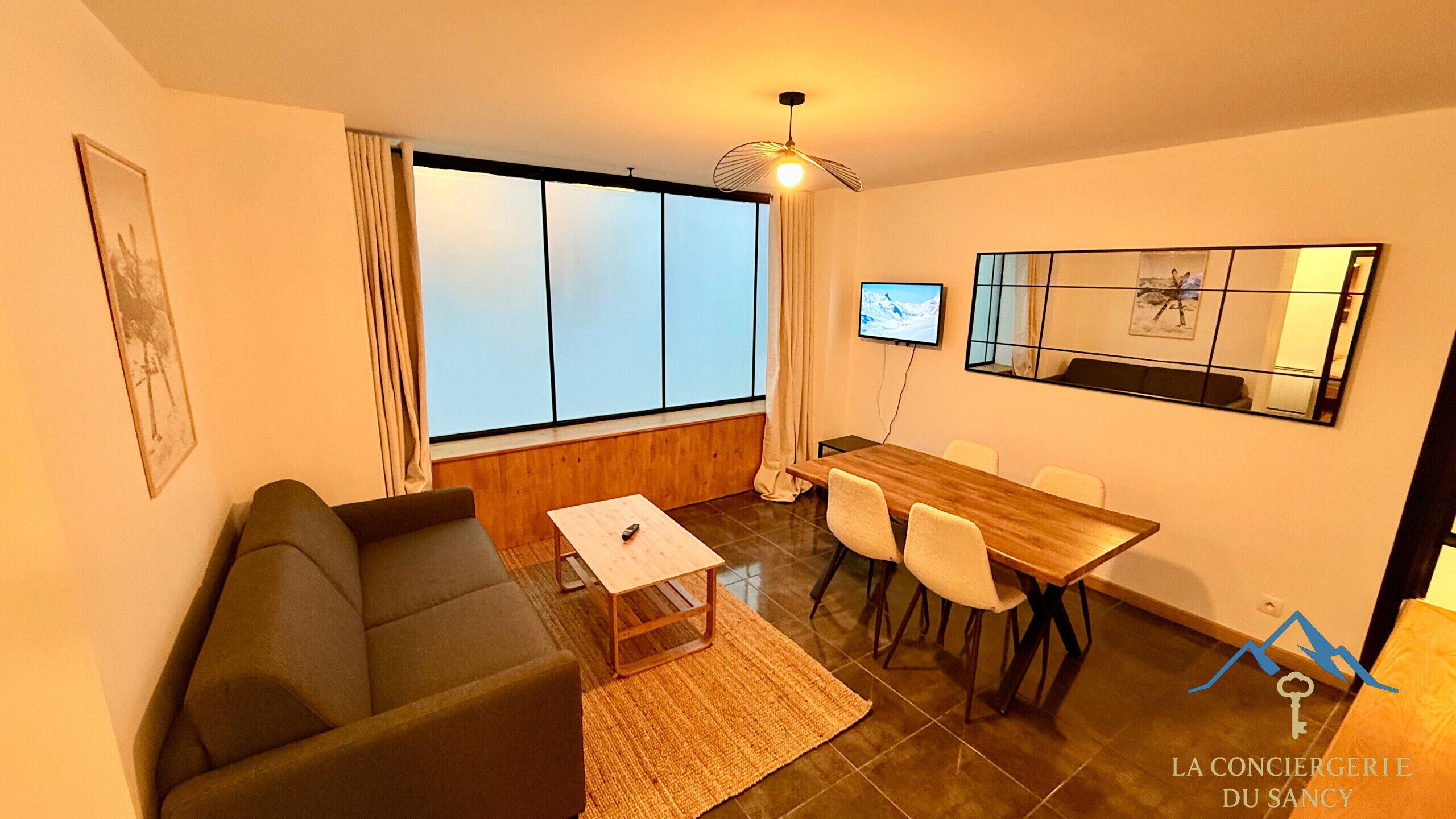 Una sala de estar moderna con un sofá, una mesa de centro, un televisor y un comedor con sillas.