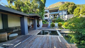 Een modern terras buiten met een zwembad, omringd door weelderige begroeiing en een berg op de achtergrond.