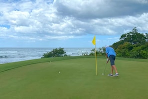 A golf course with a flagstick, a flag, and a body of water in the background. - Naka-Mar Beachfront Villa (Las Golondrinas , Hacienda Pinilla)