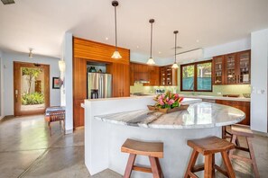 A modern kitchen with a central island, wooden cabinets, pendant lighting, and a view of the outdoors. - Naka-Mar Beachfront Villa (Las Golondrinas , Hacienda Pinilla)