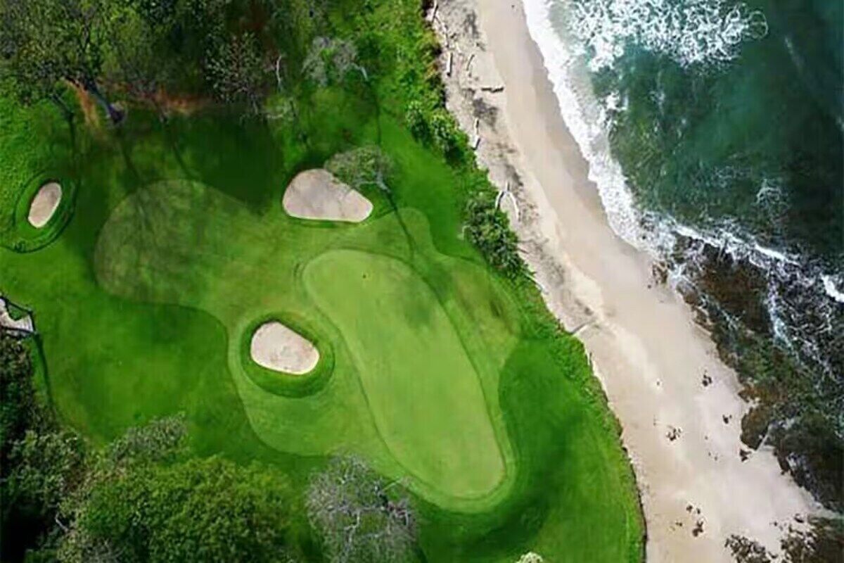 An aerial view of a golf course with sand bunkers and a beach.