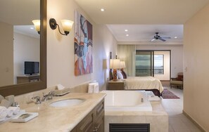 Ein Hotelzimmer mit einem großen Bett, einem separaten Badezimmer mit Badewanne, einem großen Spiegel und einem Fernseher in der Ecke.