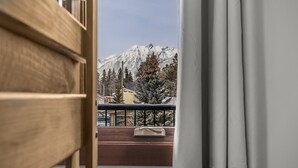 Udsigt fra en balkon med gelænder af træ, der viser et sneklædt bjerg og en bygning med gul facade.
