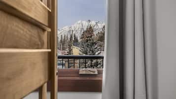 A view from a balcony with a wooden railing, overlooking a snow-covered mountain and a building with a yellow facade.