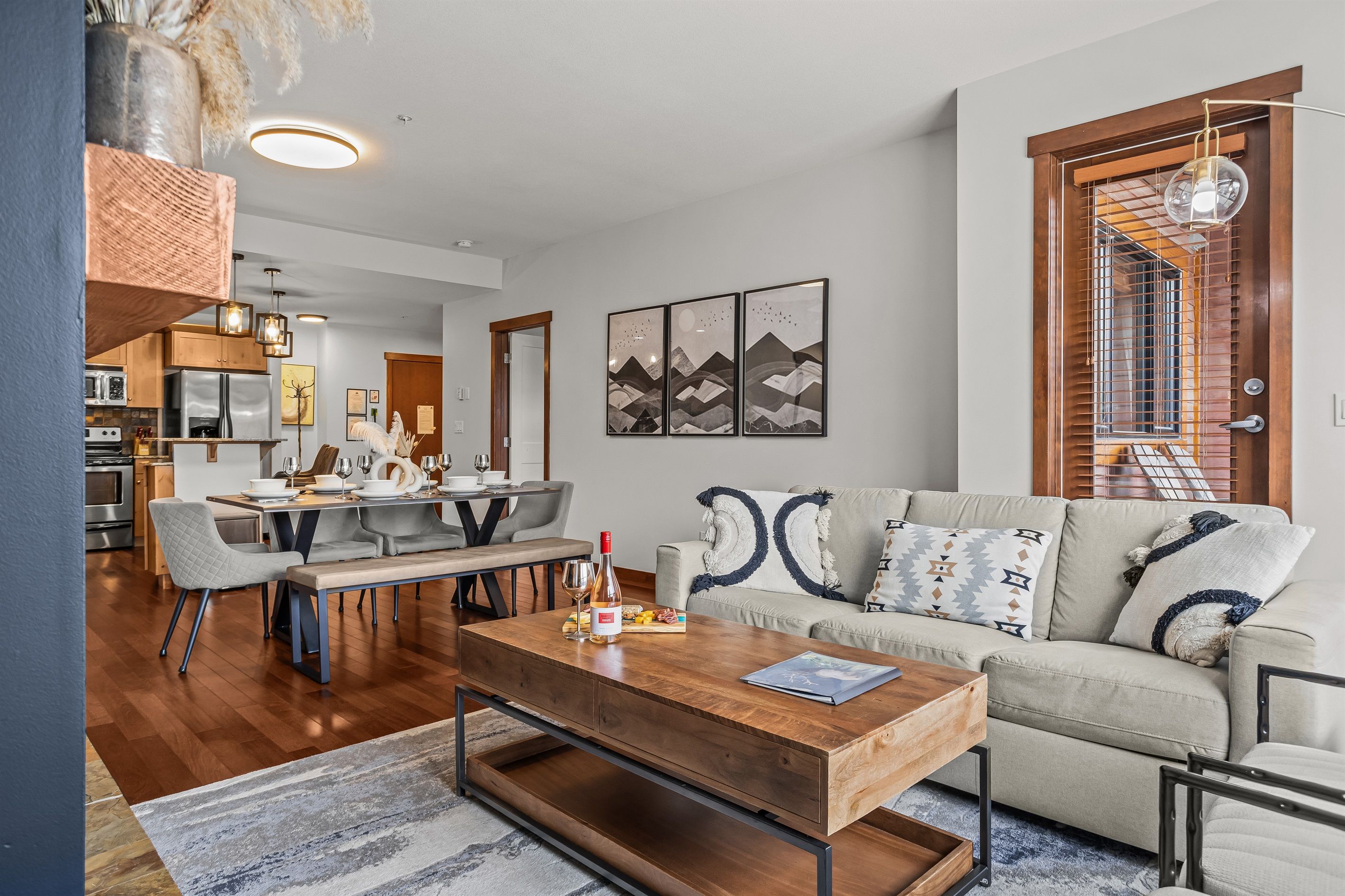 A modern living room with a wooden coffee table, a beige sofa, and a dining area with a wooden table and chairs.