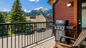 En balkon med grill, udsigt til sneklædte bjerge og en gade med parkerede biler.
