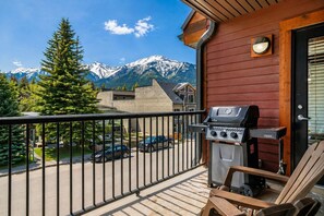 A balcony with a grill, a view of snow-capped mountains, and a street with parked cars. - Downtown |Sleeps 10 | Walk to shopping | Restaurants| Creekside trails and Ponds (Canmore)