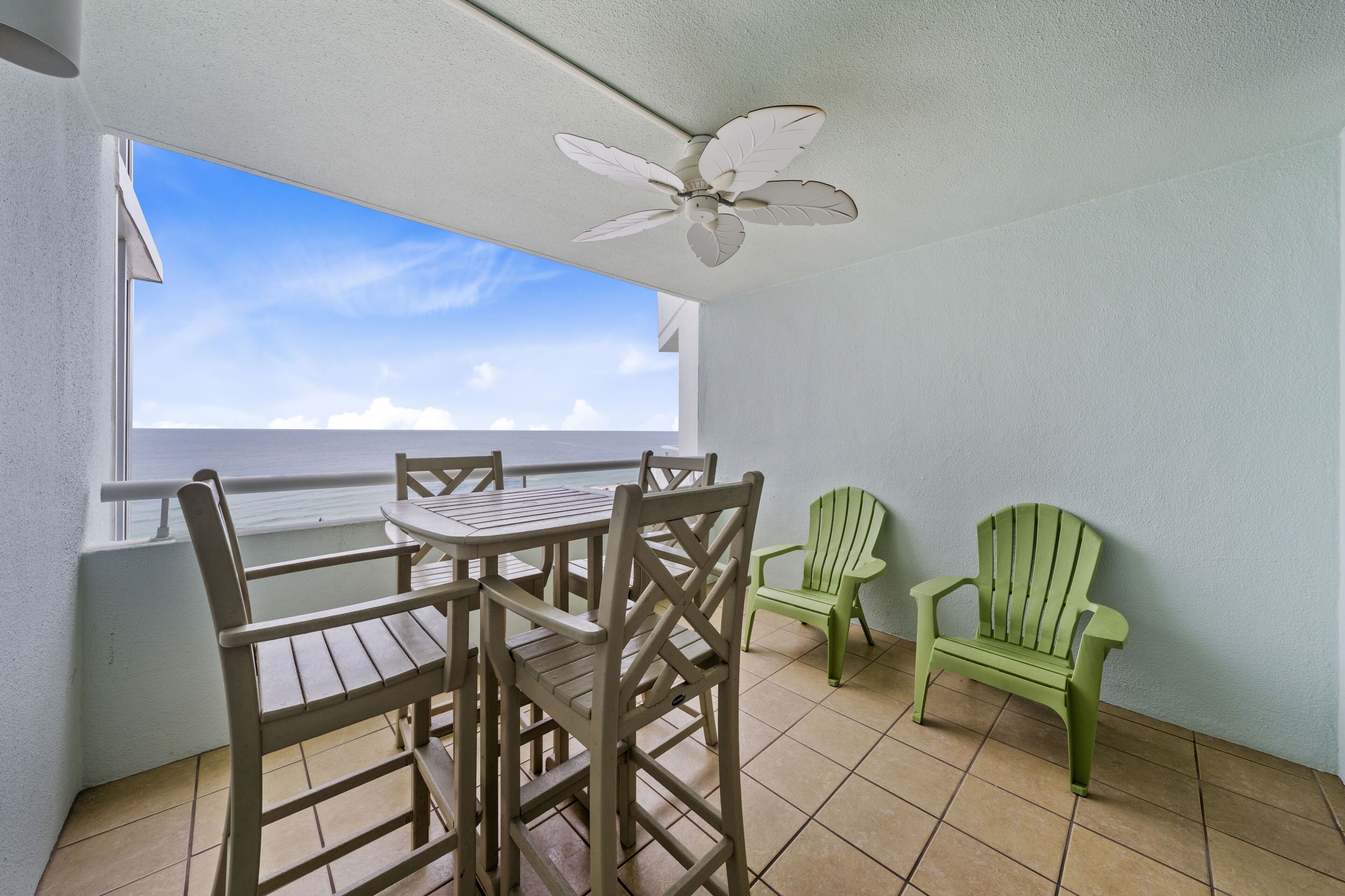 A balcony with a table and chairs, a ceiling fan, and a view of the ocean.