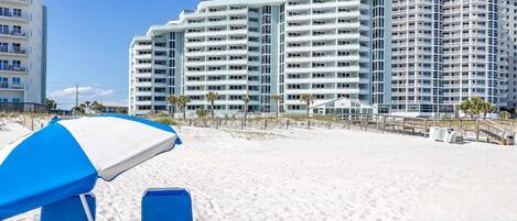 Ein Strandhotel mit mehreren Hochhäusern, einem Sandstrand und einem blau-weißen Sonnenschirm.