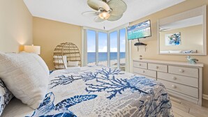 Quarto com cama, televisão, cômoda e vista para a praia.