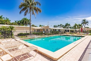 A swimming pool with lounge chairs, palm trees, and a building in the background. - Casa Mar - 28 Premium (Sarasota)