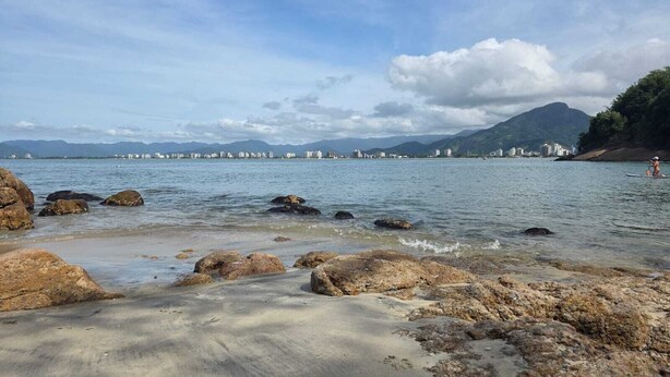 Une plage côtière avec un premier plan rocheux et une vue sur la ville en arrière-plan.