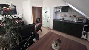 Eine moderne Küche mit Mikrowelle, Toaster und einem kleinen Kühlschrank. Es gibt einen Essbereich mit einem Holztisch und Stühlen. Im Vordergrund ist eine Topfpflanze zu sehen.