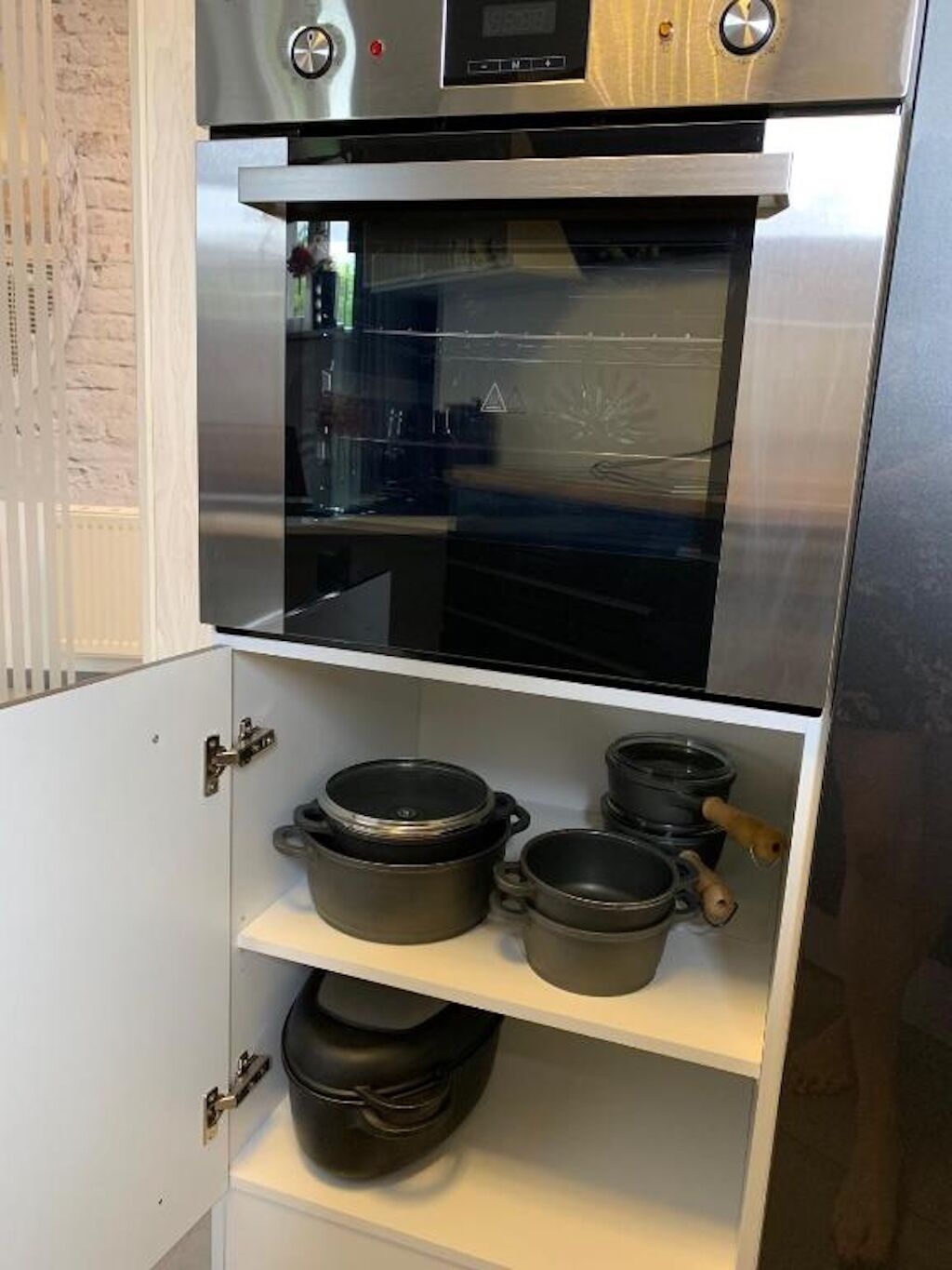 Una cocina con horno de acero inoxidable, microondas y horno de puerta de vidrio. Hay tres ollas en el estante inferior.