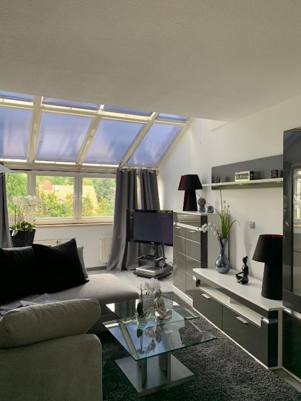 A modern living room with a glass coffee table, a sofa, a flat-screen TV, and a skylight.