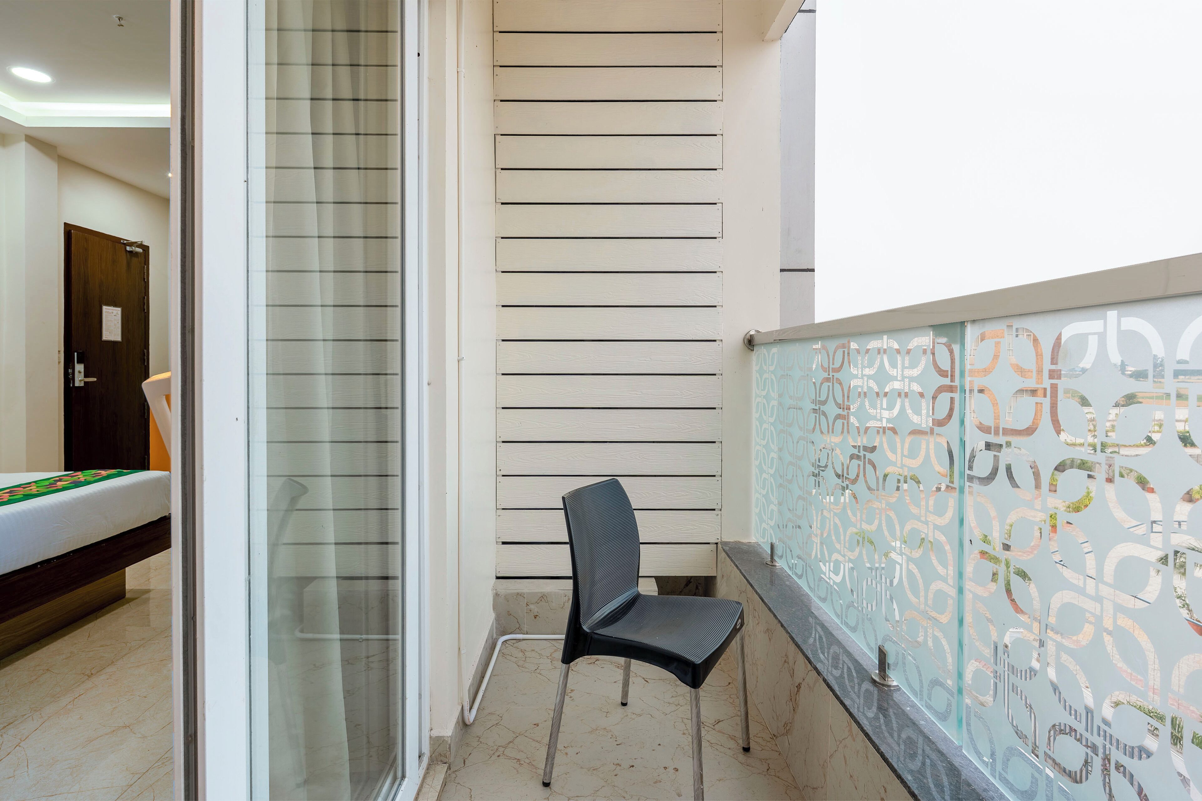 A small, enclosed balcony area with a single black chair, a glass door, and a patterned glass partition.