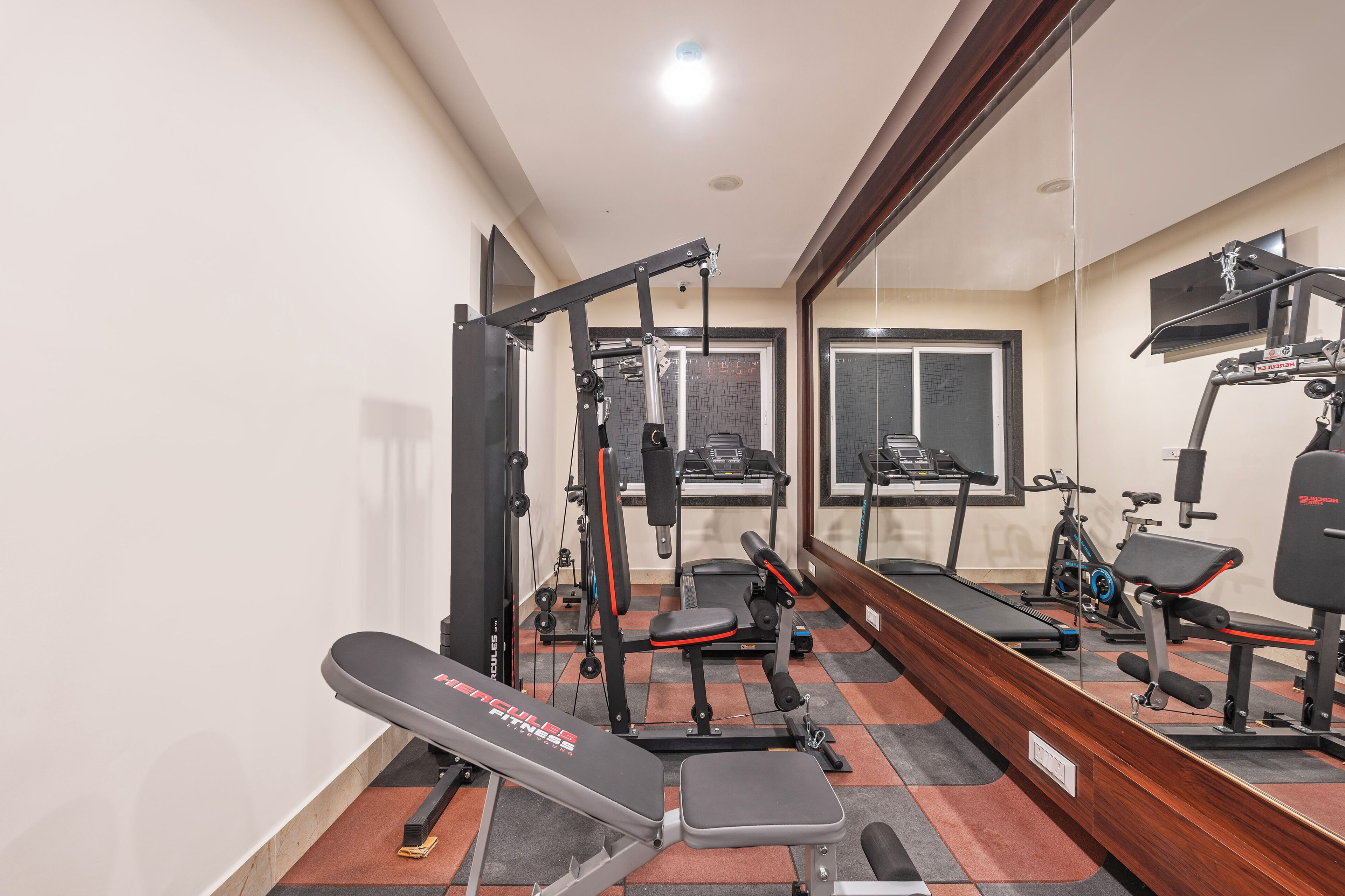 Et fitnesscenter med forskellig træningsudstyr, herunder bænkpres, squat rack og løbebånd.