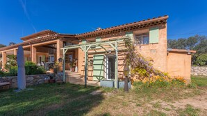 Ein Haus mit überdachter Terrasse, einer Steinmauer und einem blühenden Garten.