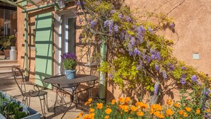 Eine Terrasse im Freien mit Tisch und Stühlen, einem grünen Tor und blühenden Pflanzen.