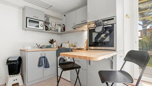 Eine kompakte Küche mit Mikrowelle, Backofen und Spüle. Ein kleiner Hocker und ein Stuhl sind vorhanden.