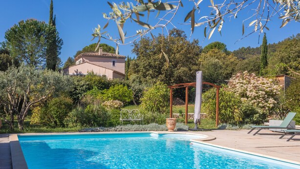 Ein Schwimmbecken mit einer Pergola, Liegestühlen und einem Haus im Hintergrund.