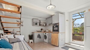 Ein kleines Zimmer mit Bett, Küchenzeile, Waschmaschine und Blick durch eine Tür.