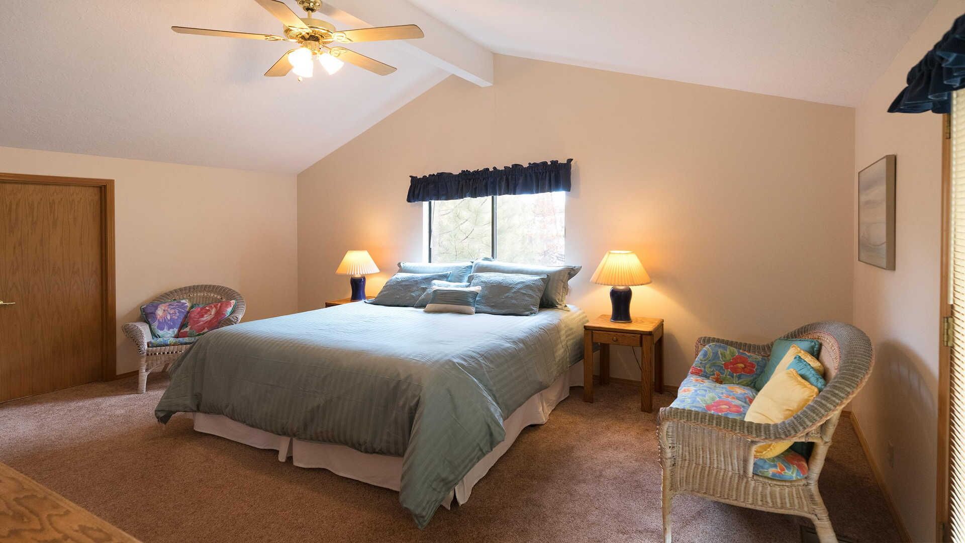A bedroom with a bed, two bedside tables with lamps, a chair, a ceiling fan, and a window with curtains.