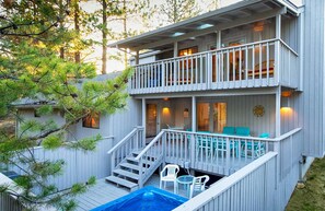 Una casa de madera de dos pisos con balcón, mobiliario exterior y un jacuzzi.