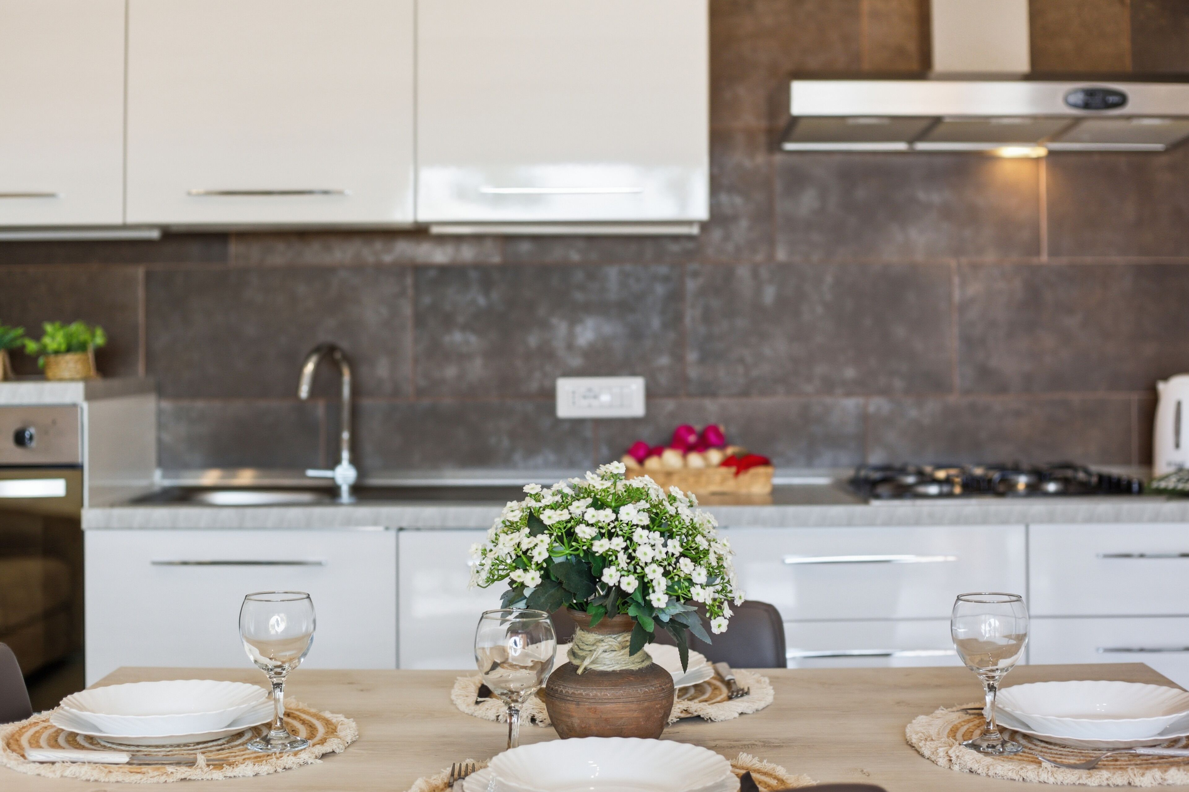 Een moderne keuken met witte kastjes, een RVS-spoelbak en een eethoek met een tafel gedekt voor twee personen.