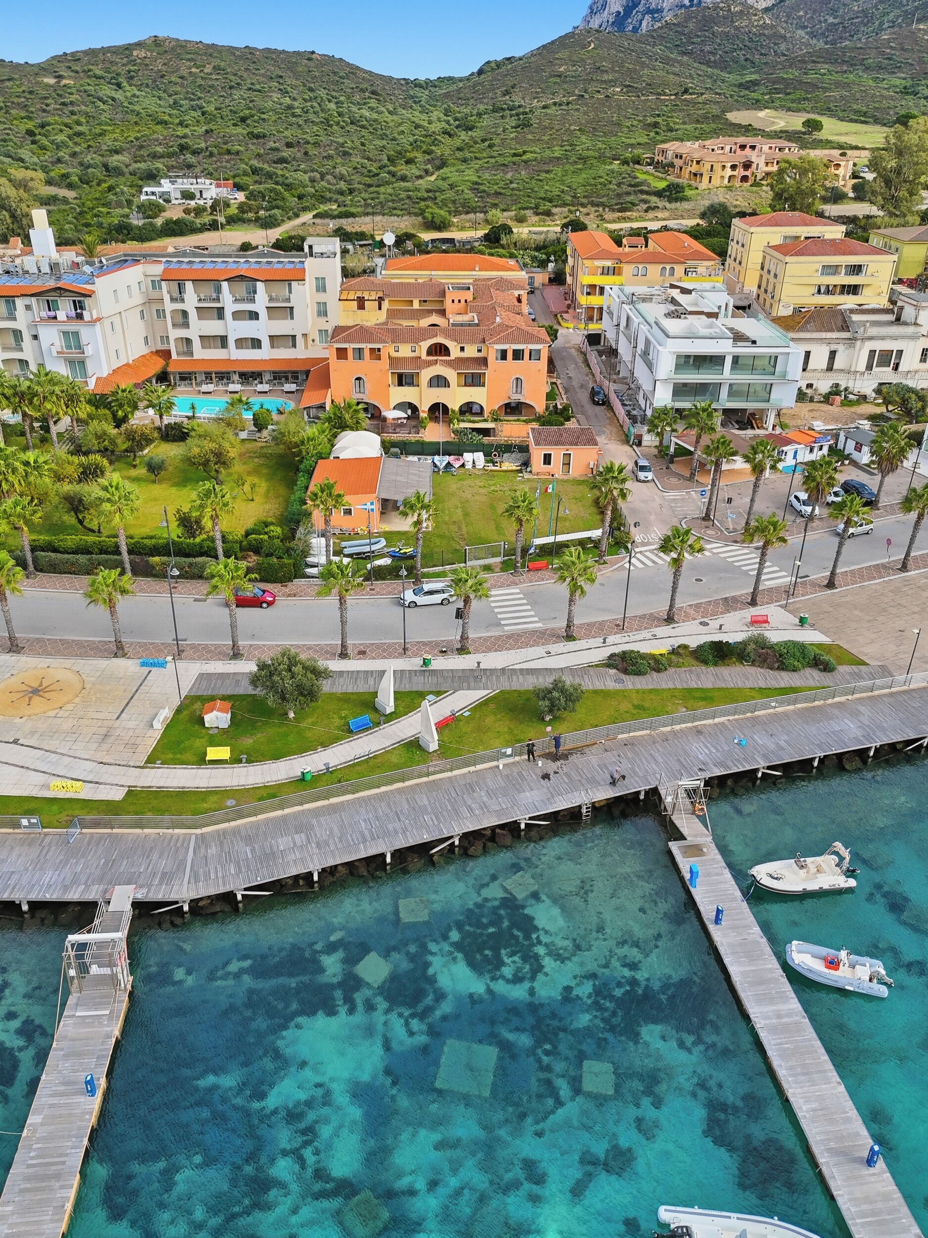 Una cittadina costiera con un porto turistico, edifici dai tetti rossi e una vista limpida sul mare.