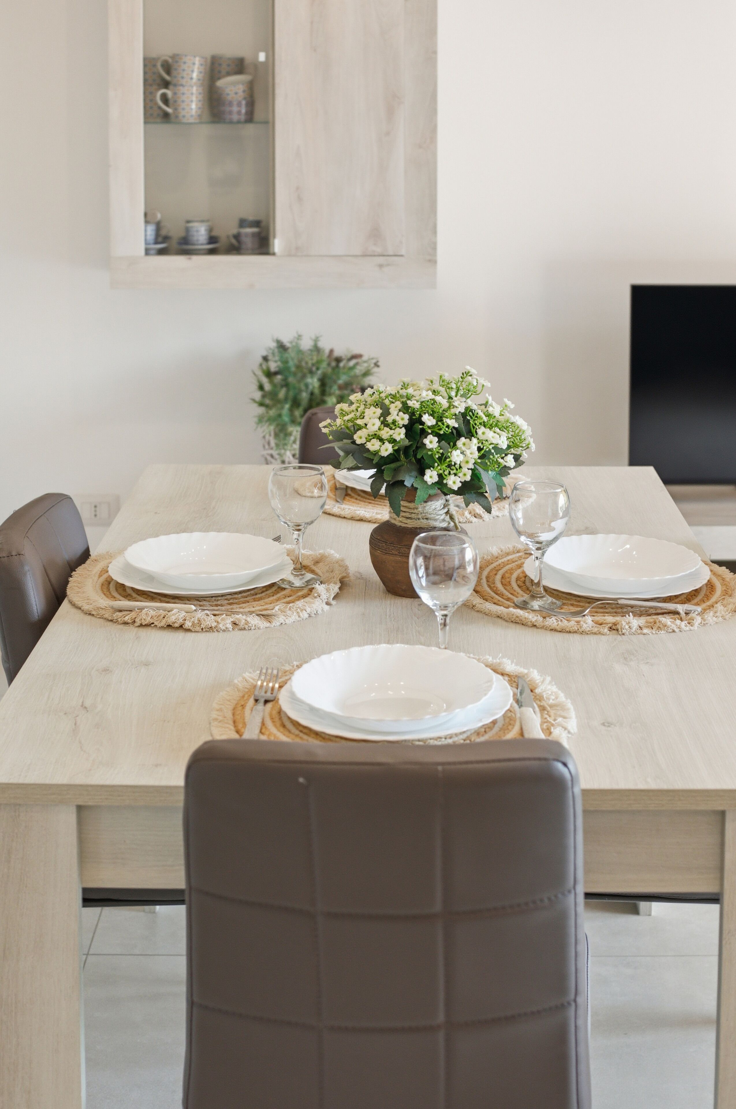 A dining table set with plates, glasses, and a vase of flowers.