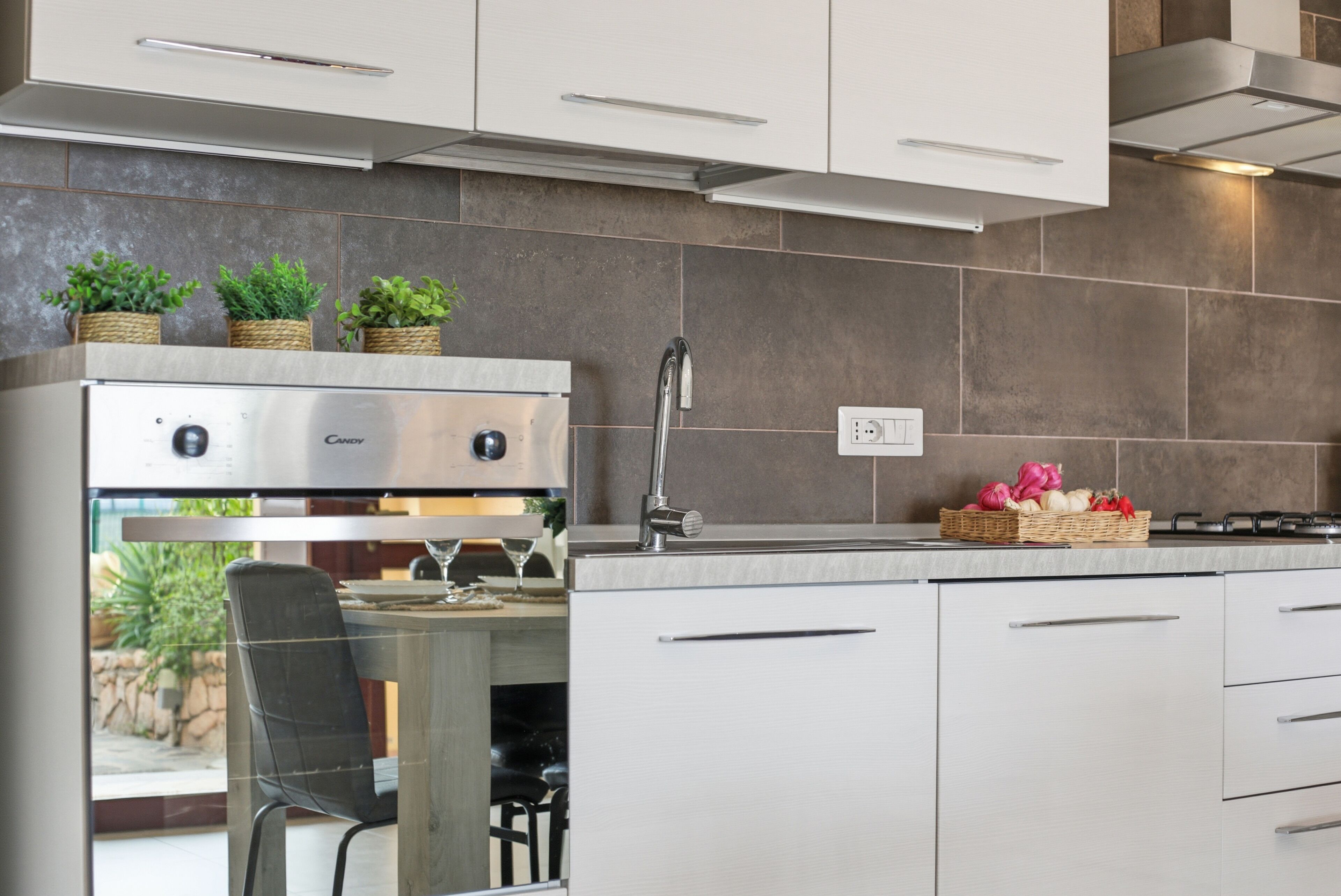 Una cocina moderna con horno empotrado, armarios de acero inoxidable, un lavamanos y ventana con vistas a un jardín.