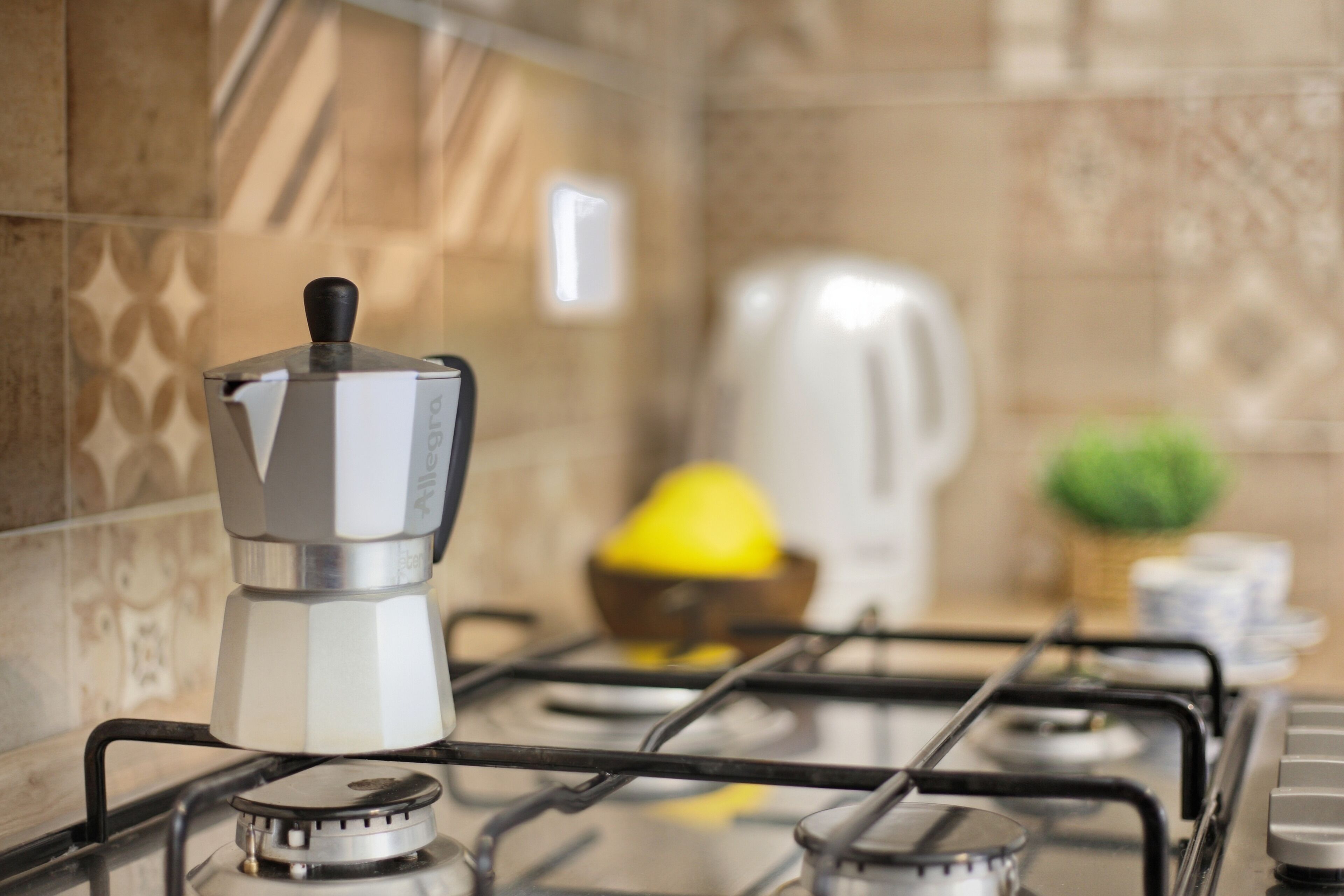 A kitchen with a gas stove, a coffee maker, a kettle, and a lemon on the counter.