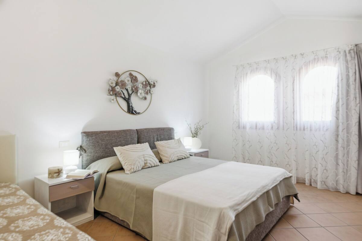 A bedroom with a bed, nightstands, a wall decoration, and a window with curtains.